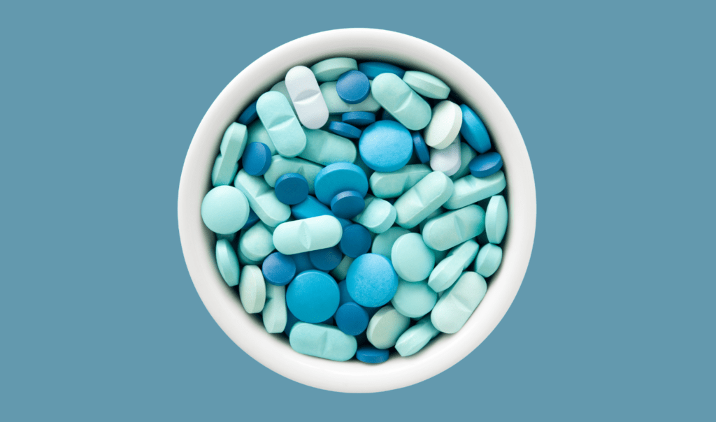 Pharmaceuticals end up in our water stream and impact marine life. The image shows a white bowl filled with pills in different hues of blue.