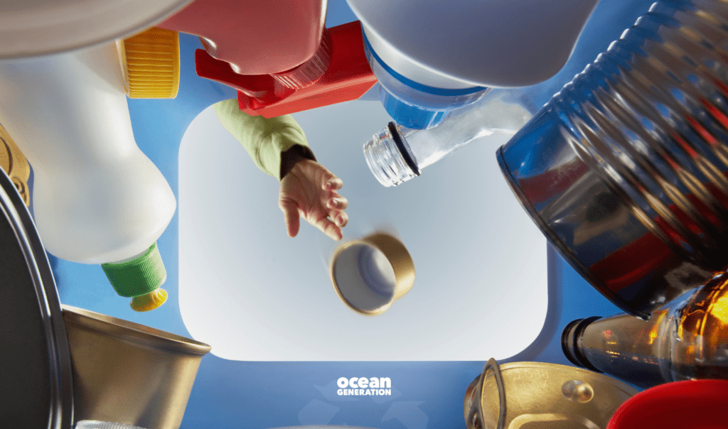 View from inside a recycling bin: A hand is visible, throwing something into recycling. Ocean Generation is sharing why recycling is not the solution to our plastic pollution problem. 