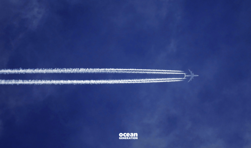 Plane flying through a navy blue sky. Behind the plane are condensation trails, also known as contrails. Ocean Generation is sharing why flying at night is worse for the environment than catching a flight during the day.