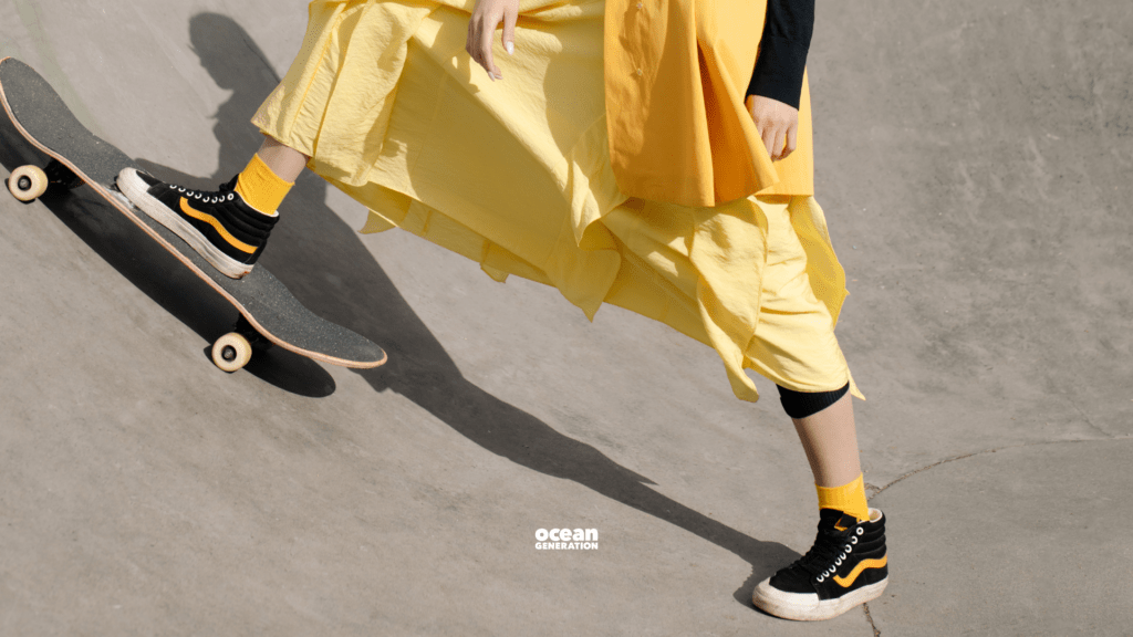 In this article Ocean Generation is sharing the impact of fashion on the environment. In this image a woman in a bright, flowing yellow dress is at a skatepark. You cannot see her face but you can see her black sneaker resting on the skateboard.