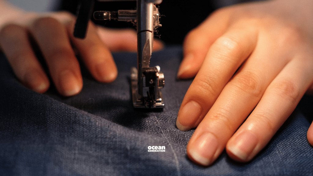 Hands working with a sewing machine. A piece of navy fabric is being transformed into a piece of sustainable fashion. Shared by Ocean Generation - experts in Ocean health since 2009.