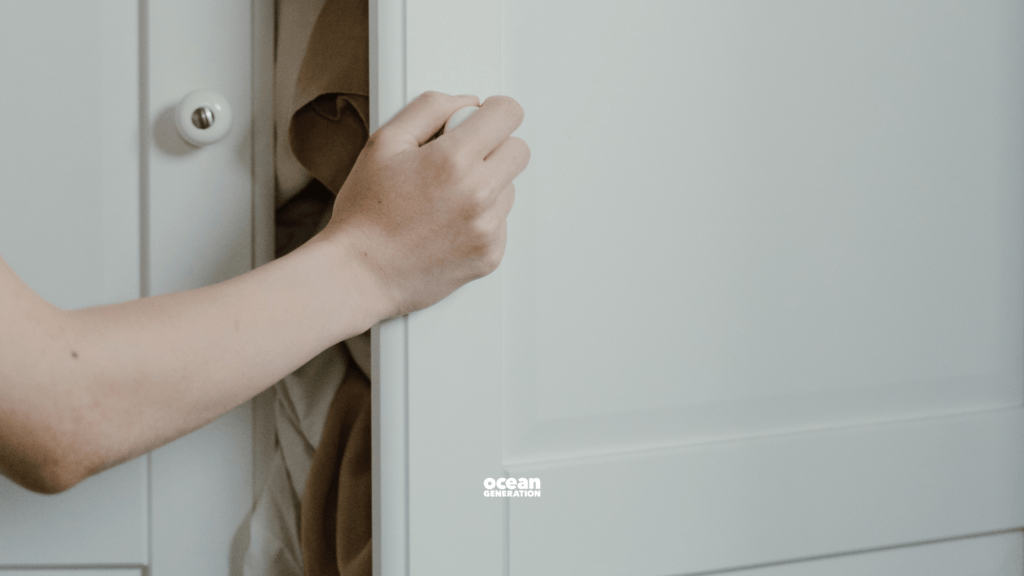 Female hand trying to force and over-full closet closed. The image symbolises our overconsumption habits when it comes to fashion and shopping.