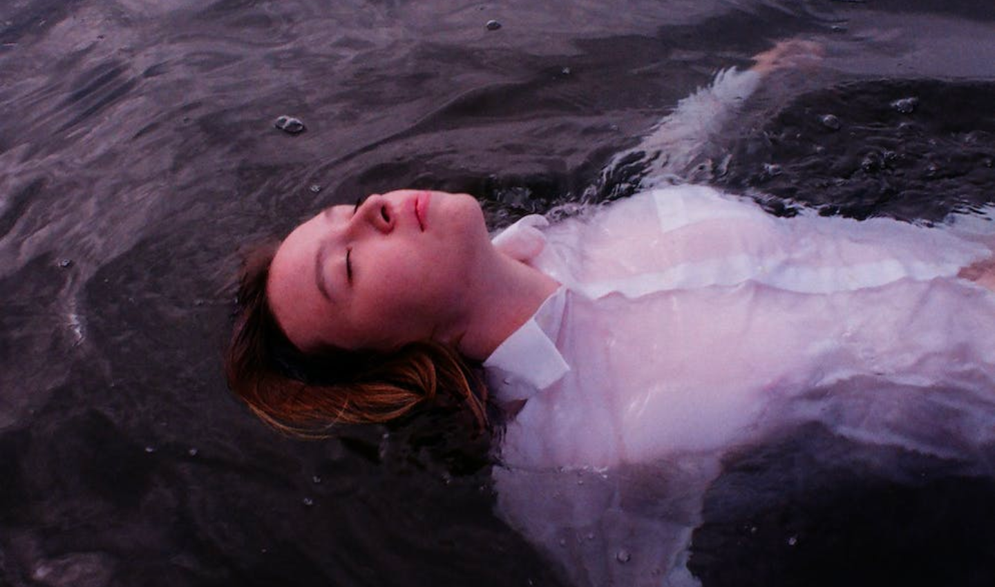 Young woman in a fashionable dress shirt floating in the Ocean. Her eyes are closed and she looks relaxed. Ocean Generation is sharing COP28 outcomes in this article with a focus on Ocean wins.